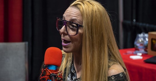 A blonde woman talking in front of a red microphone